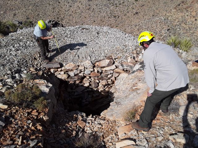 An open mine shaft half covered by wooden boards in Joshua Tree National Park, the kind that may drop straight down a hundred feet or more.