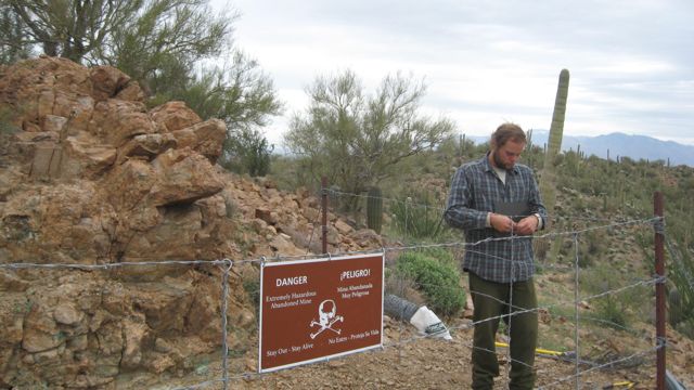 Wire fencing and a warning sign closing an abandoned mine site in Saguaro National Park, Arizona.
